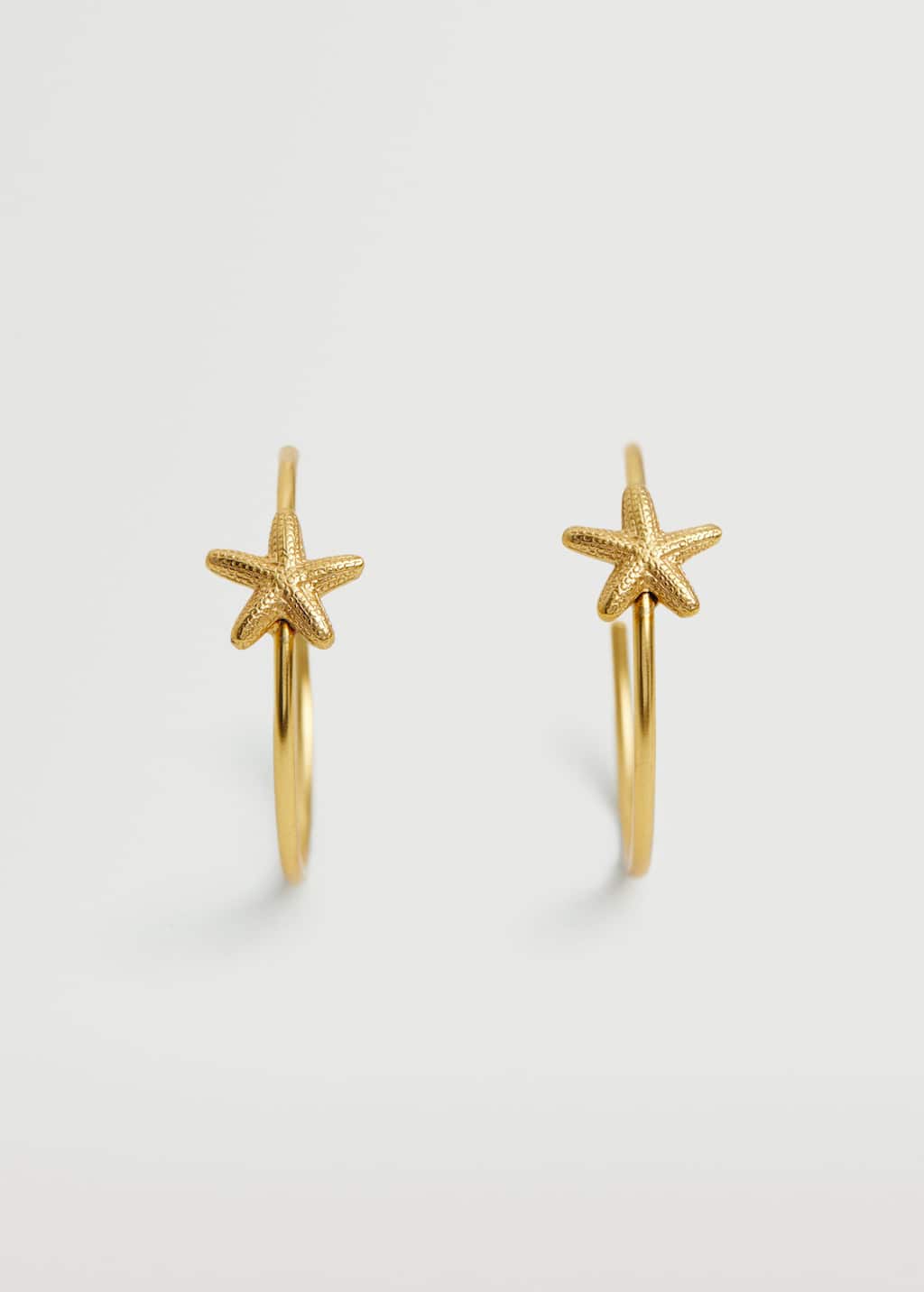 Los clásicos aros dorados se reinventan por obra y gracia de unas simples estrellas de mar. Una forma rápida de añadir un toque veraniego a tus accesorios para el día a día. Pendientes dorados de Zara (12,99 euros)