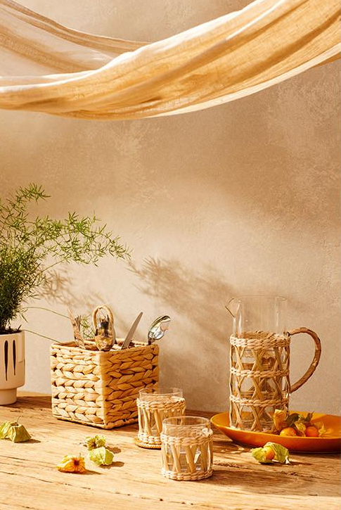 Primark Home apuesta por las fibras naturales en todos los elementos deco, incluido el menaje de mesa: la jarra de cristal y ratán cuesta 10 euros y el pack de 2 vasos de ratán, 6 euros.