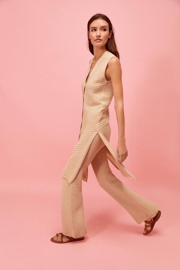 Chaleco largo en tejido de punto de algodón orgánico texturizado con estructura geométrica, manga sisa, escote de pico, cierre de botones y aberturas en el bajo, color beige. Su precio es de 49,99 euros.