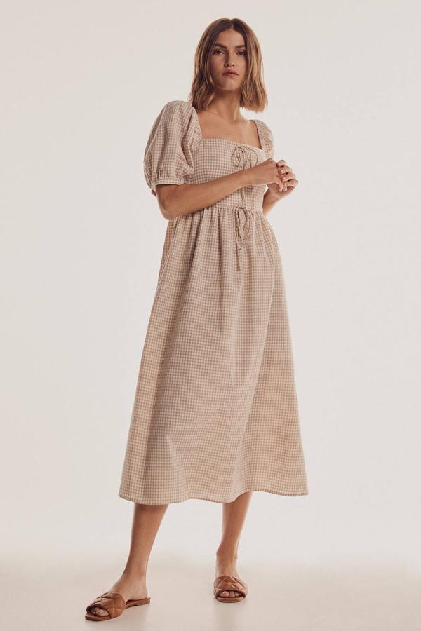 Vestido midi con escote cuadrado, manga corta abullonada, cuerpo ajustado, falda amplia con vuelo, bolsillos laterales y detalle de lazo en el pecho, en vichy beige y blanco, de Cortefiel. Su coste es de 160 euros.