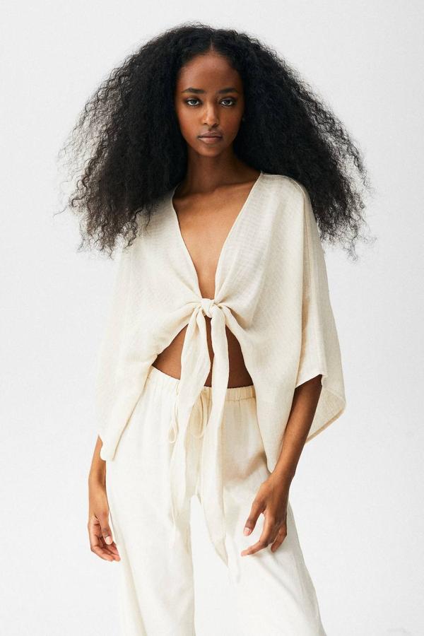 Blusa tipo kimono cropped en tejido ligero rústico con manga por debajo del codo acampanada, diseño fluido y cierre frontal mediante lazada, de Pull&Bear. La puedes encontrar en blanco, malva o con estampado étnico, por 22,99 euros.