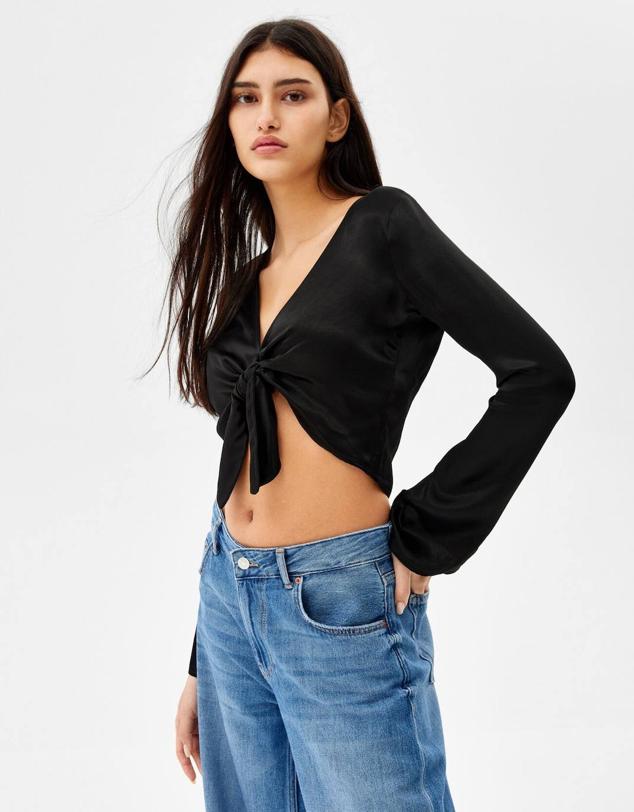 Blusa satinada cropped con escote de pico, bajo asimétrico y manga larga acampada, de Bershka. Cómprala en versión estampado retro rosa, crudo o negro, a 19,99 euros.