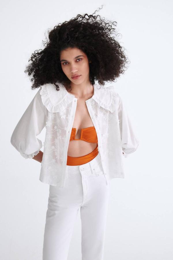 Blusa en tejido ligero con cuello bobo, manga abullonada por debajo del codo terminada en volante y detalles bordados de flores en el cuerpo, color blanco, de Zara.