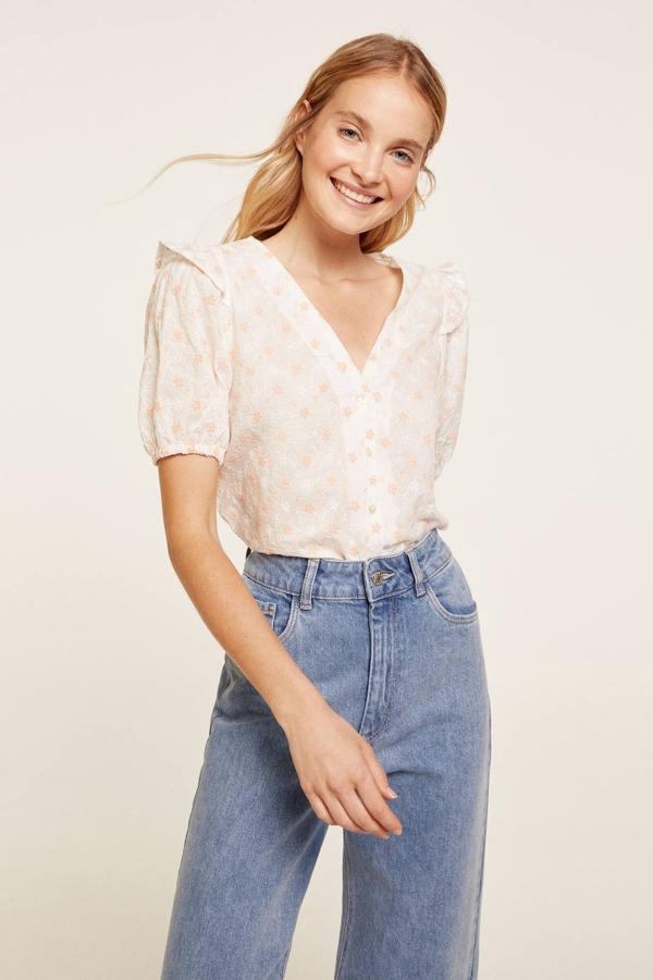 Blusa en tejido ligero con bordados de flores estilo suizo, escote de pico, cierre delantero de botones, manga corta abullonada terminada en elástico y volantes en los hombros, color blanco, de Springfield. Está disponible ahora por 19,99 euros.