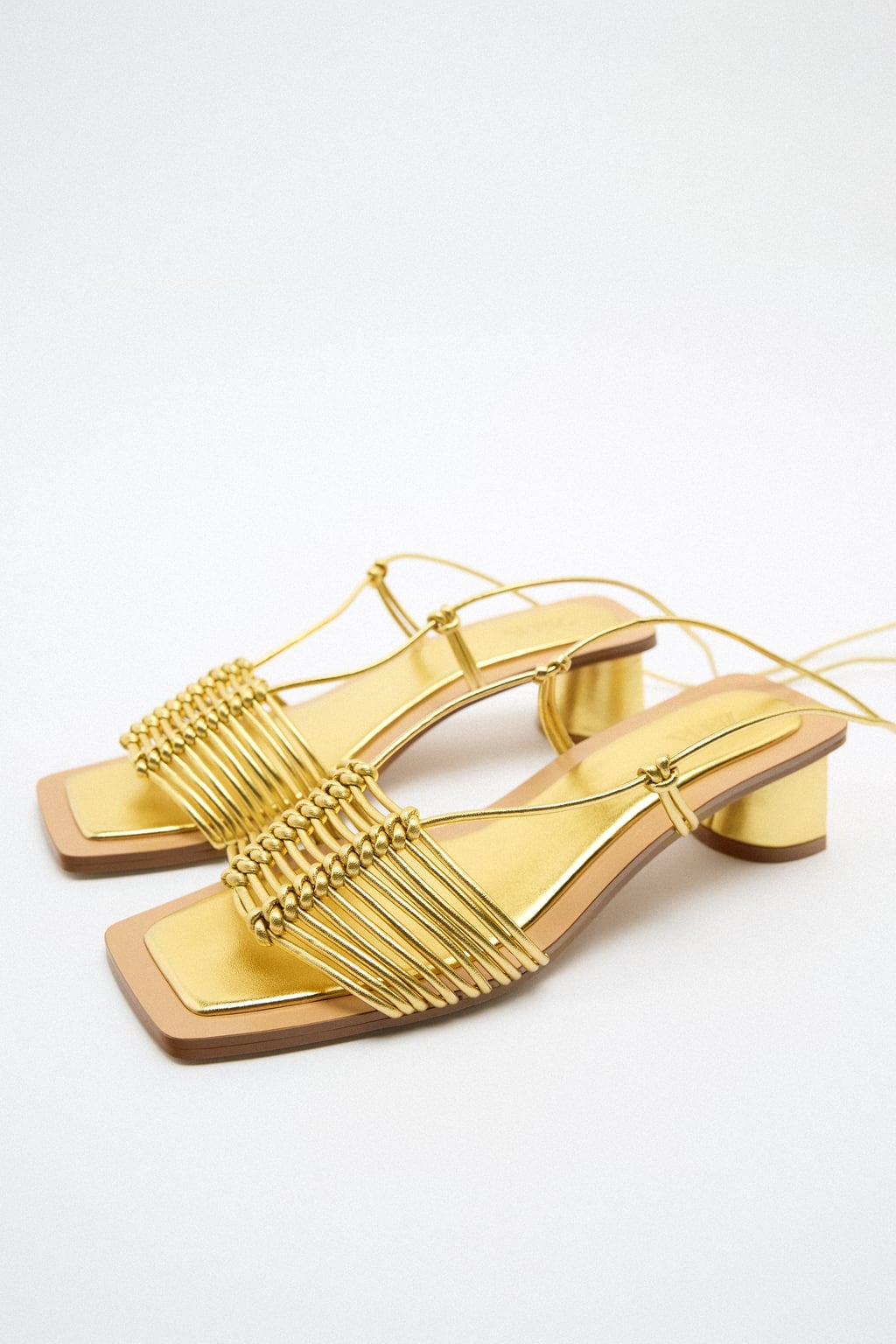 Un diseño a medio camino entre la comodidad de la sandalias plana y los tacones de infarto. Sandalias doradas con tiras de Zara (45,99 euros)