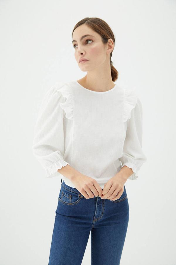 Blusa blanca en tejido texturizado con manga abullonada tres cuartos, cuello redondo y detalles de volantes, de Cortefiel. Tiene un precio rebajado de 12,99 euros.