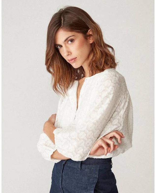 Blusa en tejido brocado semitransparente con hilo metalizado, manga francesa abullonada y cuello de pico, en blanco, de Naf Naf. Está disponible en El Corte Inglés, rebajada por 36,90 euros.