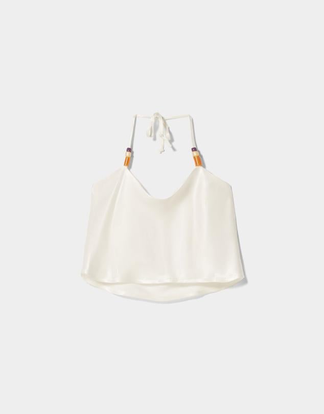 Top crudo satinado con unos bonitos detalles de abalorios. Es de color crudo con tirantes muy finos ajustables. Ideal para llevarlo con la barriga y espalda al descubierto. Es de Bershka. Precio: 15,99 €.