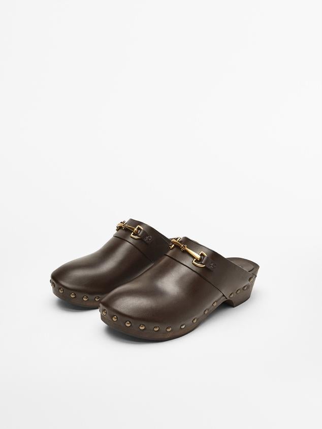 Zueco color marrón con diseño destalonado. Posee un detalle con aplique metálico. Además, tiene el logo grabado en talonera con un detalle de tachas en el corte. El tacón mide unos 4 cm. Es de Massimo Dutti. Precio rebajado: 49,95 €. 