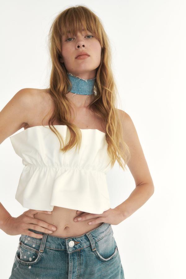 Top bandeau de escote recto de color blanco roto. Su diseño voluminoso es idóneo para llevarlo con pantalones pitillos o de corte recto. Es de Zara. Precio: 15,95 €. 