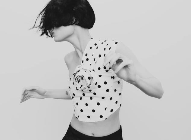 Top con estampado de lunares, escote asimétrico con un solo tirante y adorno de flor en relieve, en blanco y negro. Cuesta 22,95 euros.