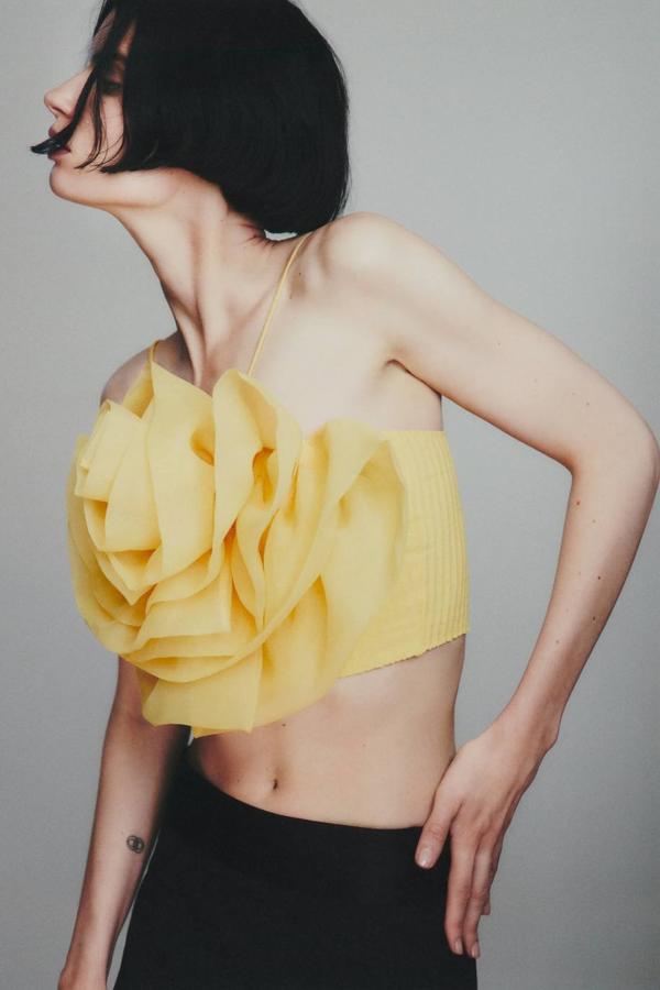 Top crop con tirantes finos, escote recto y detalle de maxi flor con volumen en tejido de organza a tono, color amarillo claro. Puedes comprarlo a 19,95 euros.