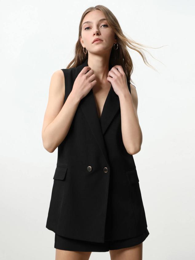 Traje compuesto por chaleco largo cruzado de cuello solapa y bermuda fluida con detalle de pinzas, de Lefties. Está disponible en negro o arena, con un coste de 22,99 euros y 12,99 euros, respectivamente.