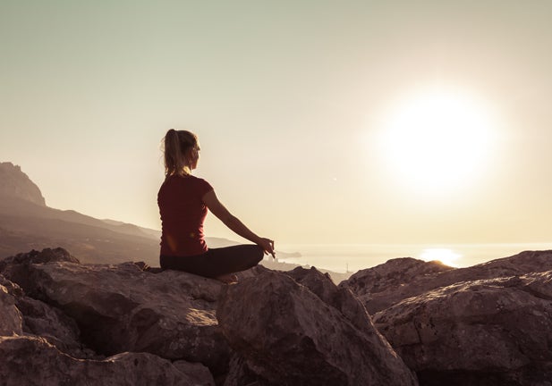 Young woman practices yoga and meditates on the mountain. Ardha Padmasana exercise, meditation