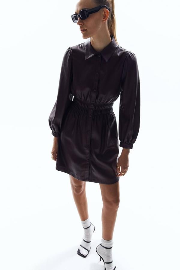 Vestido corto en tejido de polipiel con cuello solapa, manga larga acabada en puño, detalle de fruncido elástico en la cintura y cierre de botones frontal, de Sfera. Lo puedes encontrar en negro o vino, por 39,99 euros.