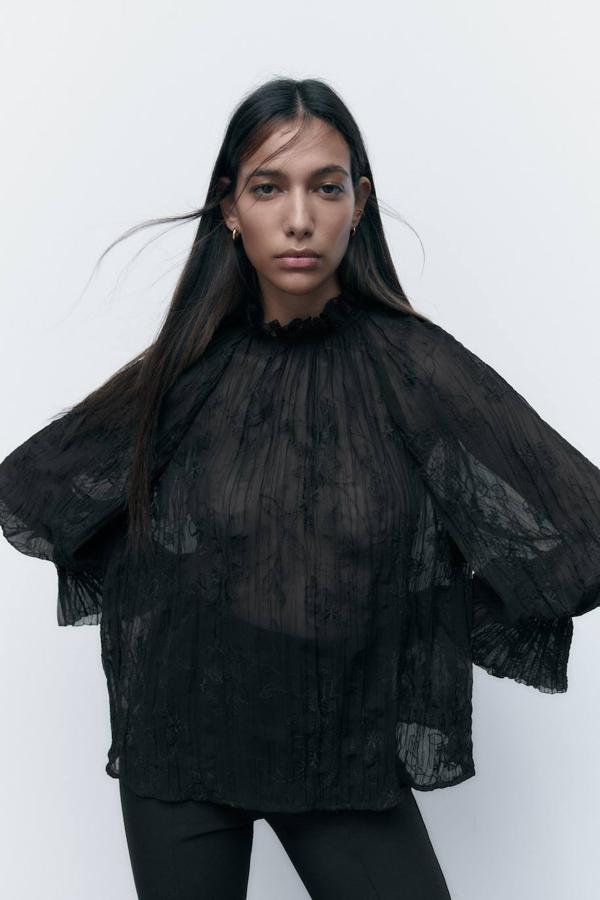 Blusa en tejido ligero con detalles bordados a tono, silueta relajada, corte amplio, mangas largas abombadas, cuello subido y volantes, color negro, de Zara. Cuesta 35,95 euros.