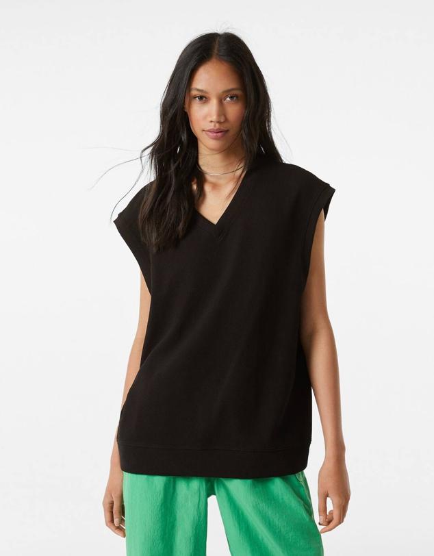 Chaleco de punto oversize con diseño amplio y largo, manga sisa y escote de pico, color negro, de Bershka. Tiene un precio de 17,99 euros.