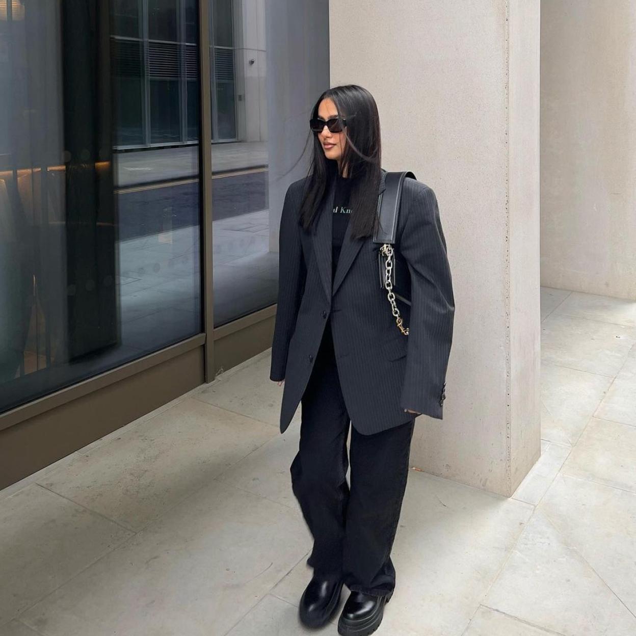 La influencer Davina Kareer con un traje negro y unos mocasines negros. 