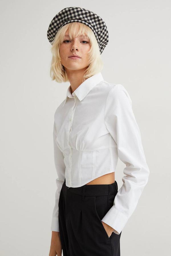 Camisa cropped de estilo corsetero en tejido de algodón con cuello solapa, mangas largas, cierre de botones y cintura entalla con pinzas y detalles fruncidos en el pecho, color blanco, de H&M. La encontrarás por 14,99 euros.