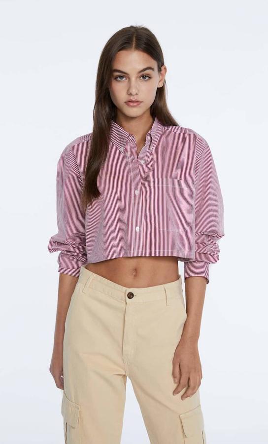 Camisa cropped de popelín con silueta relajada, manga larga, cuello solapa y bolsillo de parche, en estampado de rayas rojas, de Stradivarius. Está disponible por 17,99 euros.
