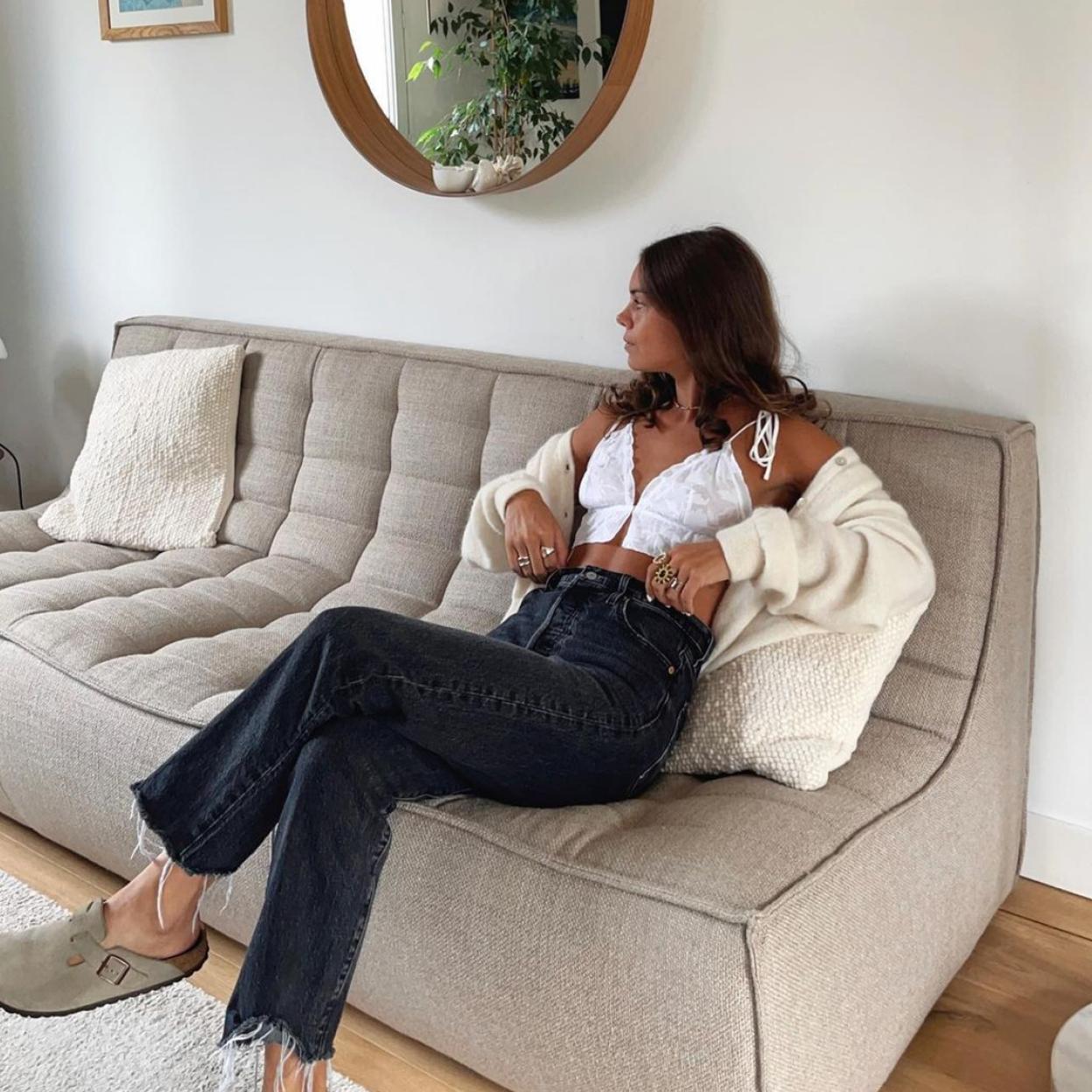 La influencer lleva un pantalón vaquero y un top blanco que combina con una rebeca de punto y unos zuecos de color marrón grisáceo. 