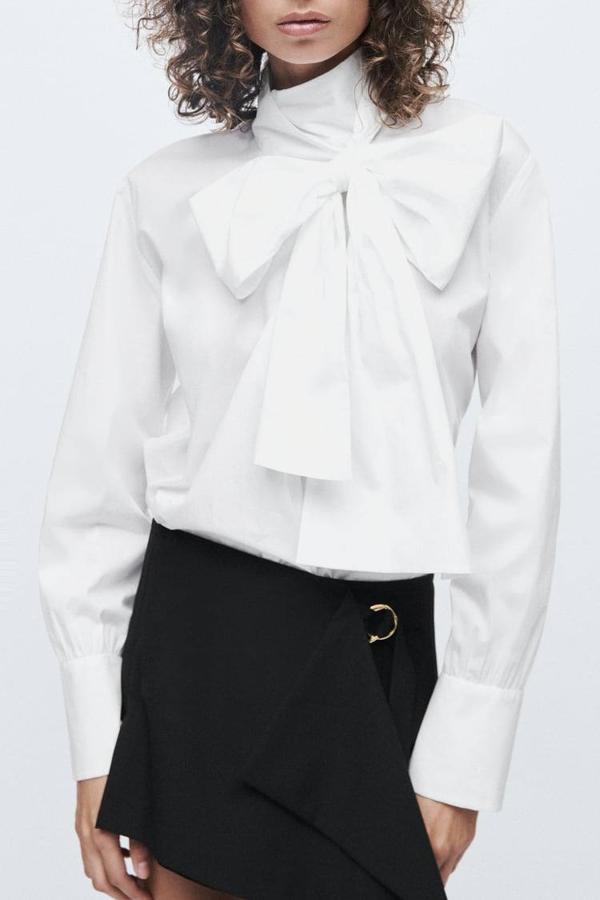 Camisa de popelín con cuello alto, detalle de lazada cruzada, manga larga acabada en puño ancho y ligeramente acombada, color blanco, de Zara. Cuesta 39,95 euros.