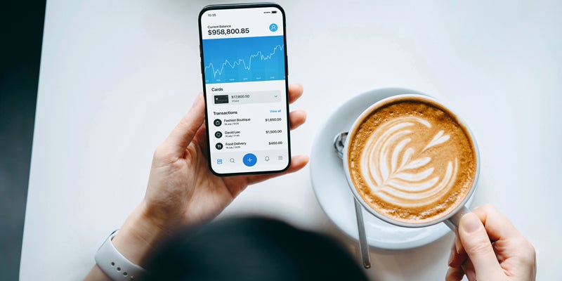 Overhead view of young woman enjoying a coffee break, managing finance and investment, checking financial stock market data on smartphone in cafe. Smart banking with technology