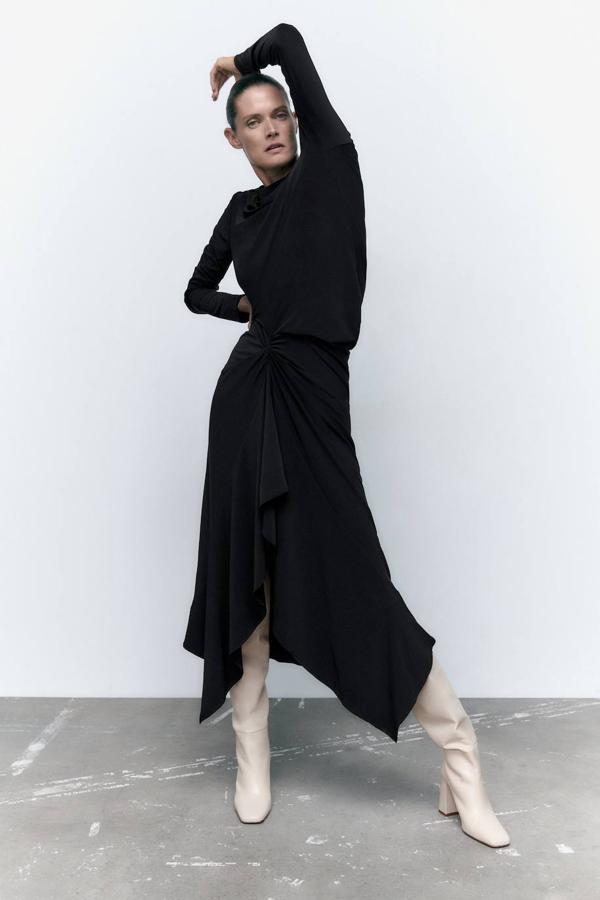 Vestido midi fluido con detalles drapeado, falda asimétrica, cuello redondo y manga larga, en negro, de Zara. Tiene un precio de 25,95 euros.