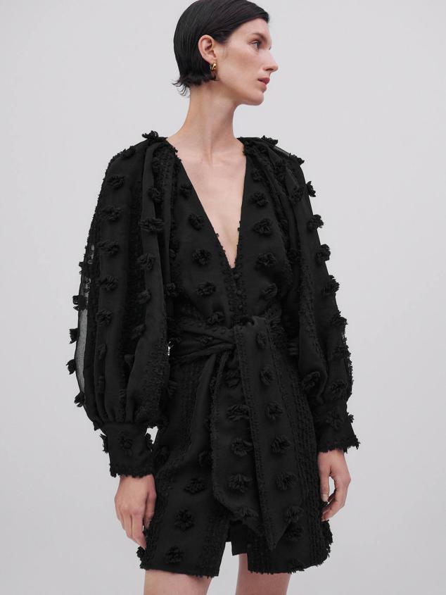 Vestido corto en tejido ligero detalles en relieve, manga larga abullonada, cinturón de lazada, abertura delantera y escote pronunciado de pico, color negro, de Massimo Dutti. Su coste es de 129 euros.