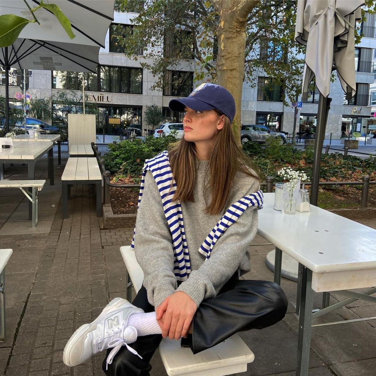 La influencer lleva una sudadera gris que combina con un jersey de rayas, una gorra azul marino y unos pantalones de cuero.