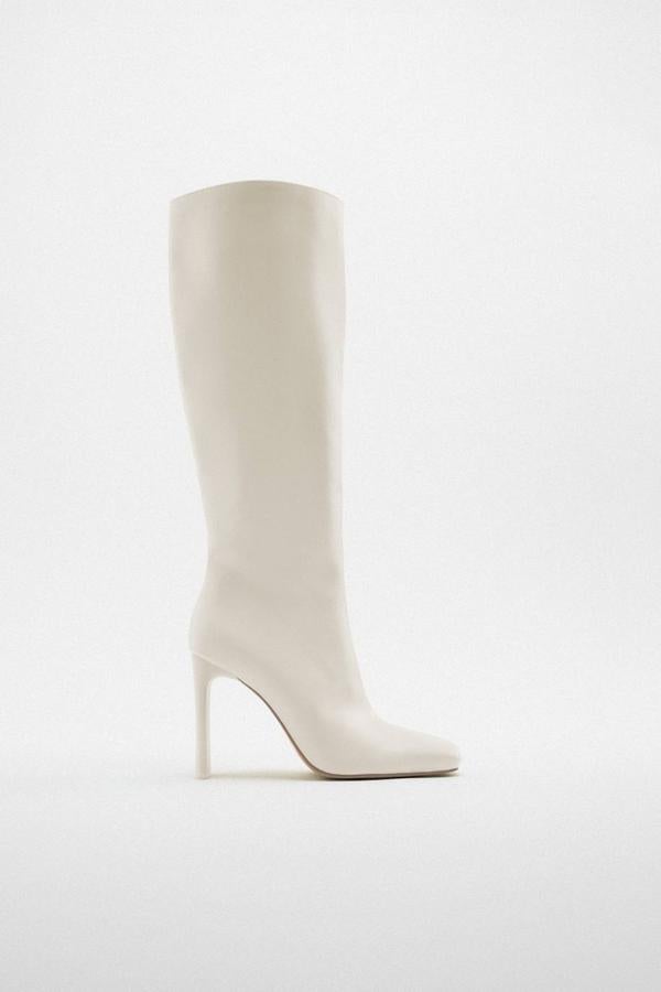 Botas altas con caña holgada, acabado brillante, puntera cuadrada y tacón plano alto, en blanco, de Zara. Tienen un coste de 49,95 euros.