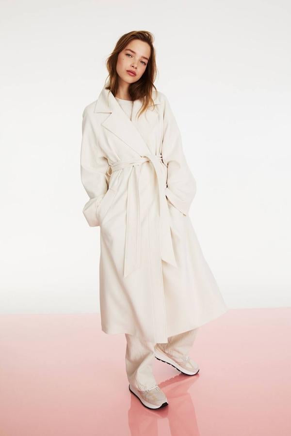 Abrigo largo de sarga con silueta relajada, manga larga, cuello solapa con muesca, bolsillos y cierre mediante cinturón de lazada a juego, color crema, de H&M. Cuesta 69,99 euros.