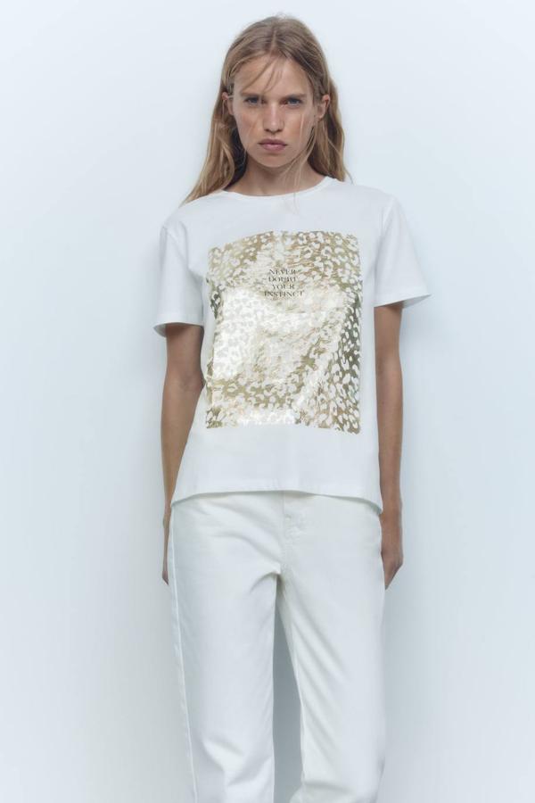 Camiseta de manga corta con cuello redondo y estampado brillante dorado con texto, color blanco, de zara. Encuéntrala por 12,95 euros.