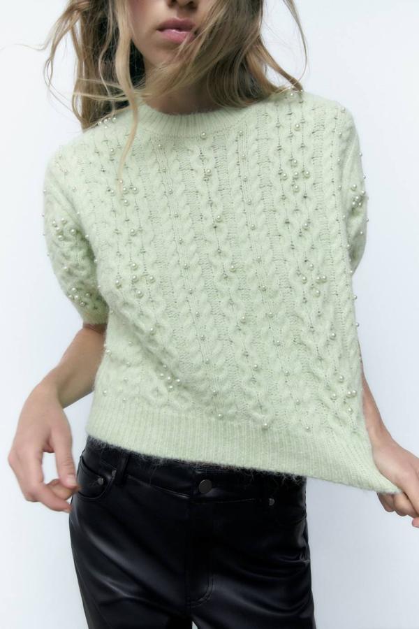 Jersey de punto trenzado con tacto suave, manga corta, cuello redondo y aplicación de perlas en el cuerpo, en tono verde pastel. Puedes encontrarlo a 29,95 euros.