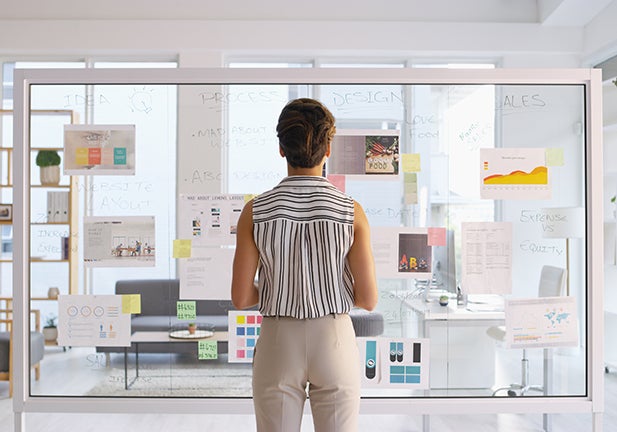 Rearview shot of a young businesswoman writing down ideas on a glass wall in her office