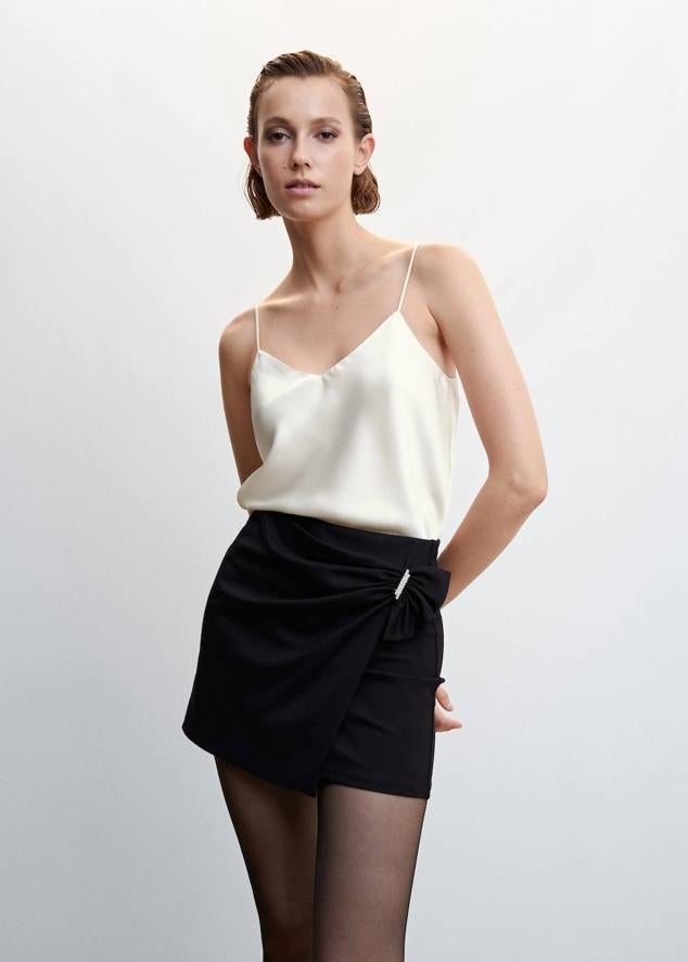 Top lencero en tejido satinado con tirantes finos y escote de pico, en tono crudo, de Mango. Tiene un coste de 17,99 euros.