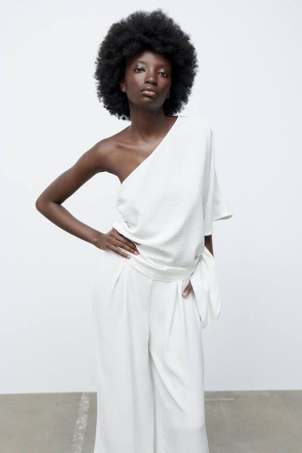Blusa con diseño asimétrico, corte fluido, manga corta ancha y detalle de nudo con lazada en el lateral, de Zara. Cuesta 19,95 euros.