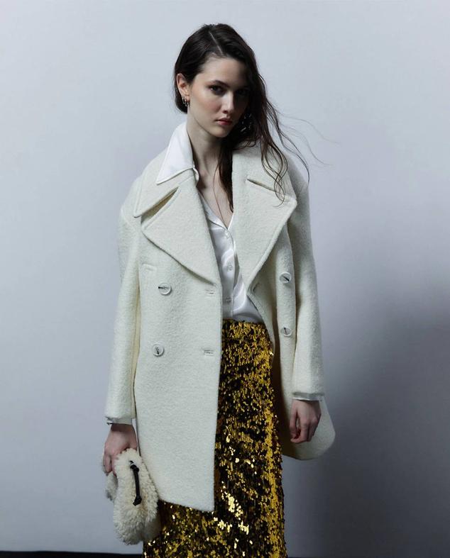 Abrigo en tejido bouclé con corte relajado, cuello solapa amplio con muesca, bolsillos y cierre cruzado, color crudo, de Sfera. Encuéntralo por 69,99 euros.