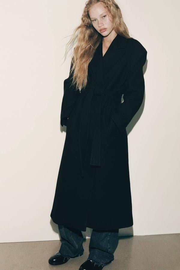 Abrigo largo confeccionado en tejido de lana con mangas largas, cuello solapa, bolsillos y cinturón, color negro.