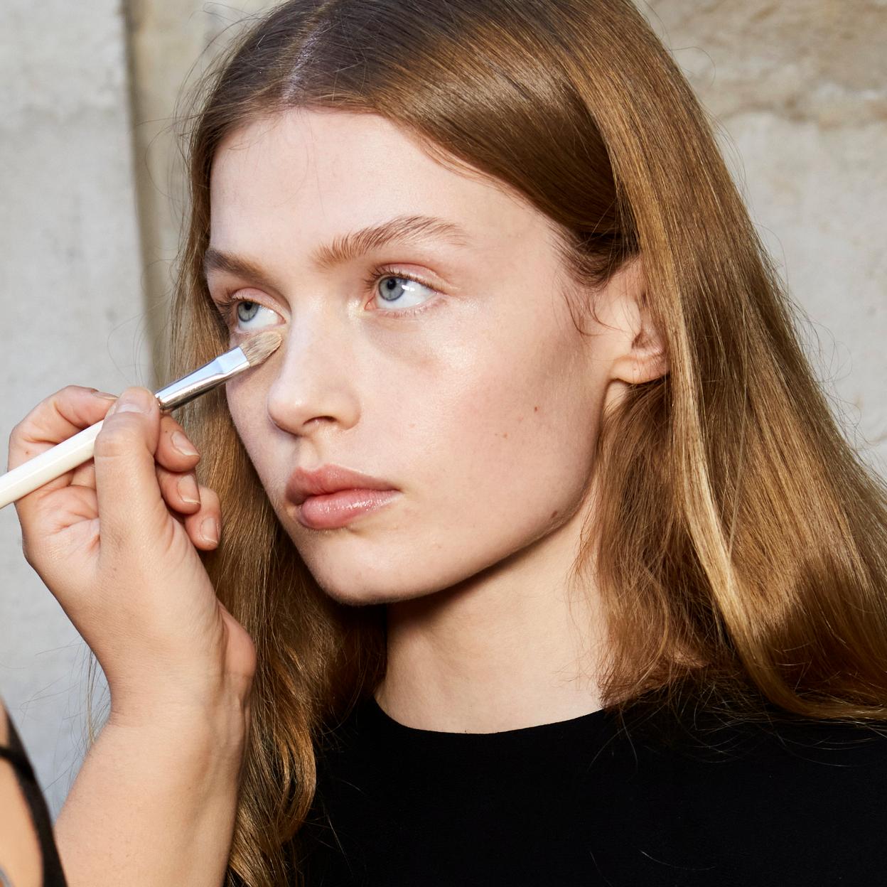 Maquilladora aplica el corrector con brocha a una modelo en el backstage.