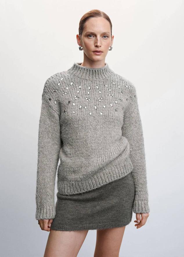 Jersey en tejido de punto grueso con cuello redondo, manga larga y detalles de pedrería, en gris, de Mango. Podrás encontrarlo a 39,99 euros, con descuento.