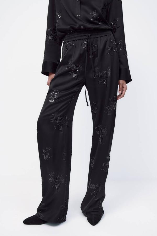 Pantalón satinado tipo pijamero con perneras rectas, tiro alto, cintura elástica ajustable y detalle de lentejuelas a tono, de Zara. Consíguelo rebajado a 29,99 euros.
