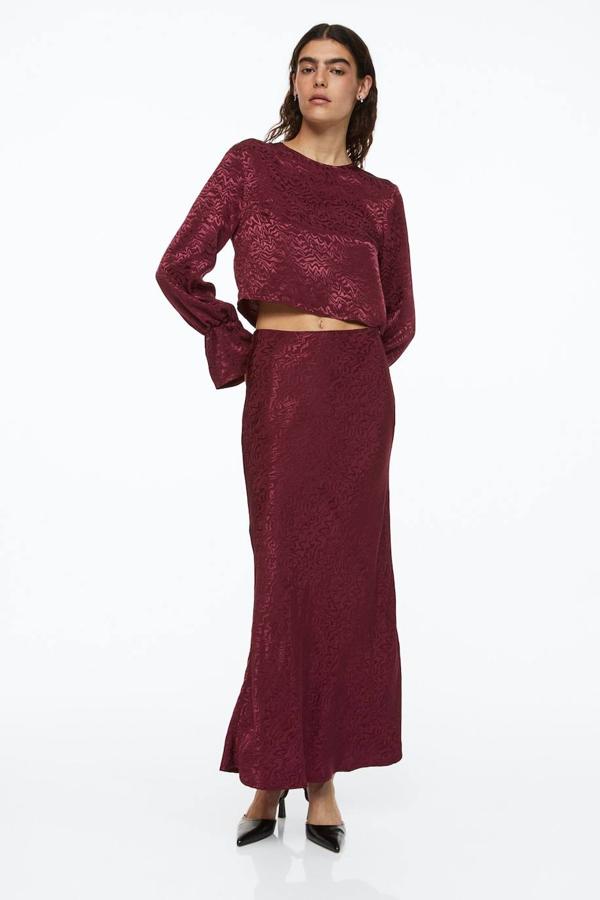Falda midi en tejido jacquard brillante con tiro alto y bajo en evasé, tono burdeos, de H&M. Encuéntrala en rebajas por 10,99 euros.