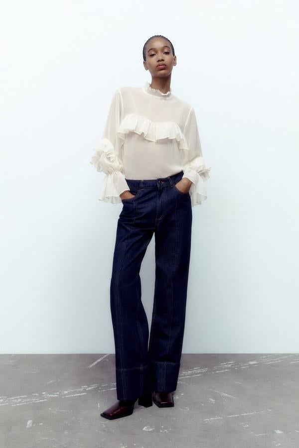 Blusa en tejido semitransparente con cuello subido, mangas largas acabadas en elástico y detalles de volantes, tono blanco roto, de Zara. Puedes comprarla en rebajas a 15,99 euros.
