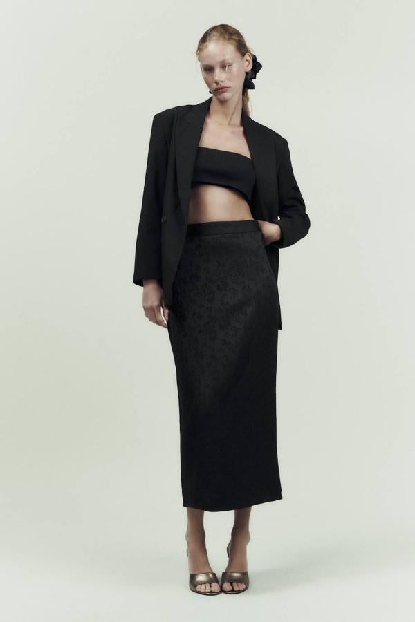 Falda midi de tubo en tejido jacquard floral con tiro alto, cintura ancha y abertura en el bajo trasero, en negro. Está disponible rebajada a 19,99 euros.