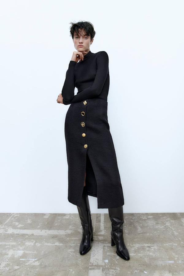 Falda midi de tubo en tejido de tweed con tiro alto, botones joya y abertura en el bajo, en negro. Puedes encontrarla rebajada por 19,99 euros.