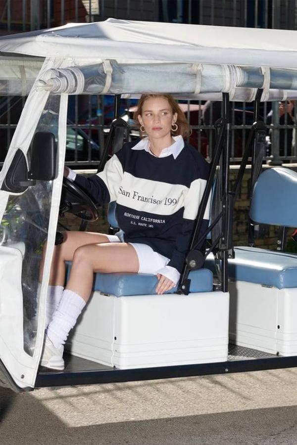 Outfit con sudadera a rayas bicolor por 25,95 euros, camisa blanca debajo, mallas y deportivas.