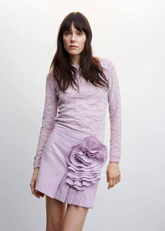 Falda corta en tejido de tweed con diseño de tablas y detalle de maxi flor plisada a juego, tono lila, de Mango. Puedes encontrarla a 45,99 euros.