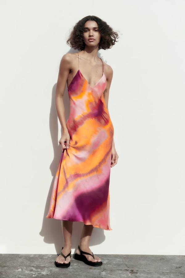 Vestido midi lencero en tejido satinado con escote de pico, tirantes finos y bajo en evasé, en estampado tie-dye tonos rosa y naranja, de Zara. Hazte con él por 35,95 euros.