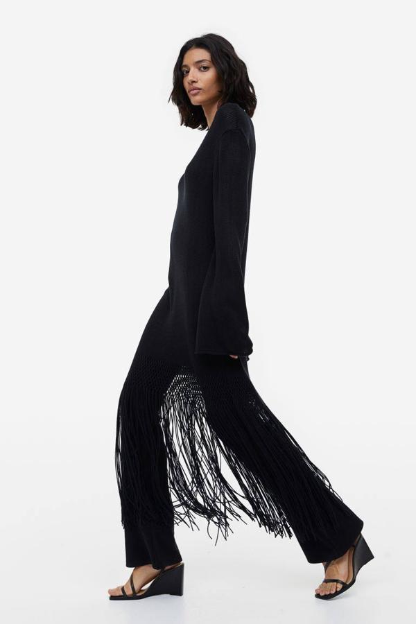 Vestido en tejido de punto con escote de pico, manga larga y bajo terminado en flecos largos a tono, color negro, de H&M. Lo comprarás por 59,99 euros.